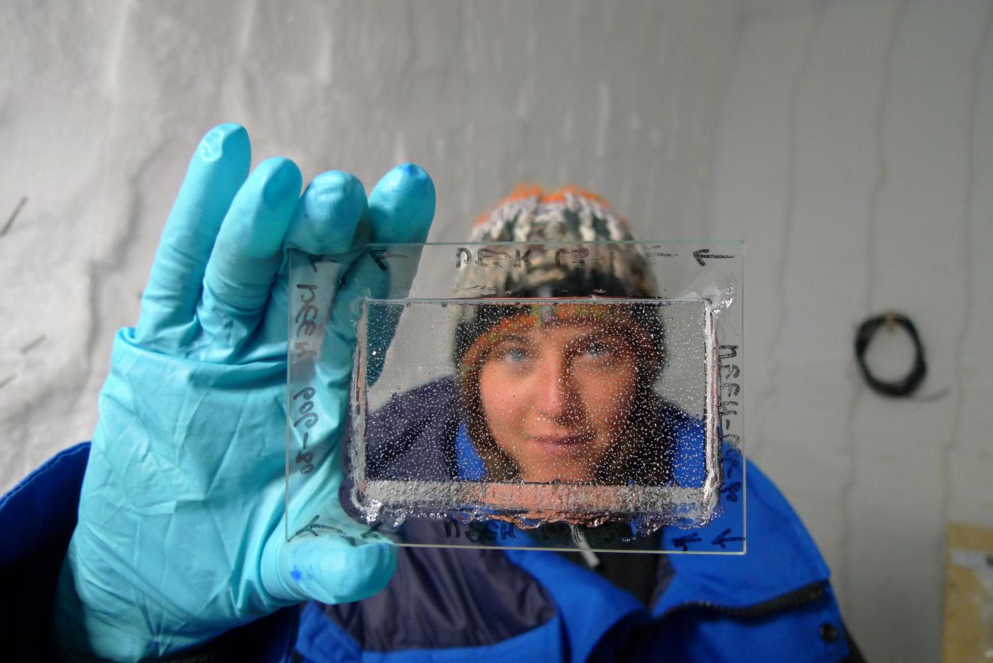 Emilie Capron looking through a thin piece of ice core with visible bubbles