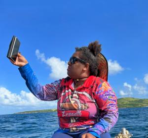 Co-researcher Lala Gutchen (NAIDOC award winner & educator/ cultural knowledge holder)  raising her phone for internet reception while taking the team out fishing