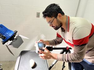 A man points a camera at a sweet potato in a laboratory setting.