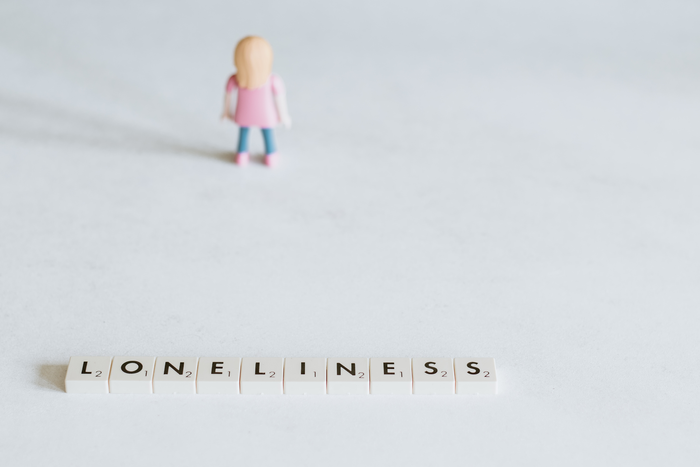 Loneliness written in crossword game letters with a plastic toy figure in the background.