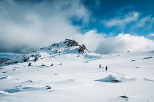 Two people walking up a mountain with snow gear