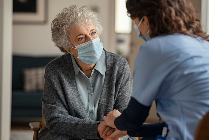 Female doctor consoling senior woman wearing face mask during home visit stock photo