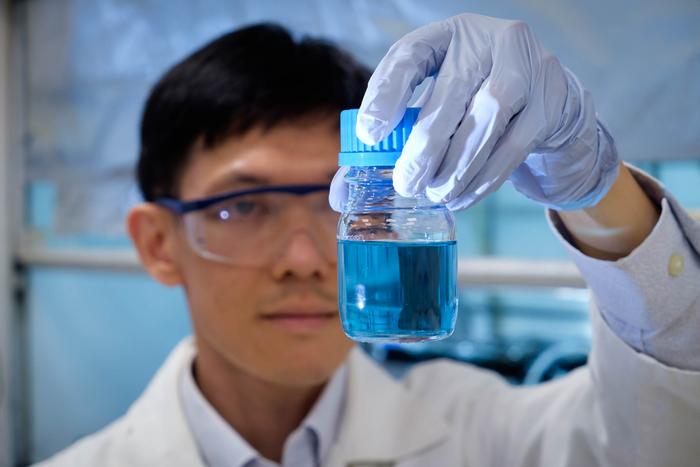 Assoc Prof Soo Han Sen looking at a bottle of solution with dissolved plastic and vanadium catalyst.