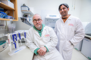 Gimenez-Lirola, left, and Rahul Nelli face the camera in a lab at the ISU Veterinary Diagnostic Lab. They wear lab coats and are surrounded by laboratory equipment.