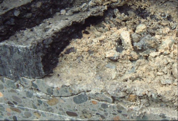 A close-up of a bridge, showing deteriorated asphalt pavement and concrete