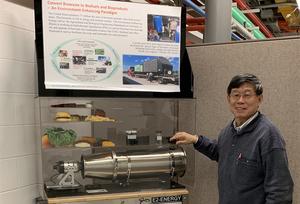 A man stands next to a display with a poster and a reactor model.