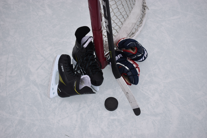 Hockey skates, puck, gloves and stick next to a goal.