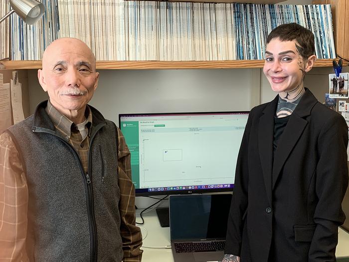 a man and a woman standing in front of a computer in an office setting