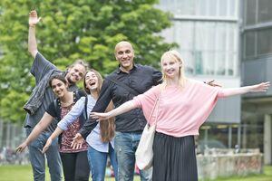 Five people with their arms stretched out in celebration in front of large tree and university building