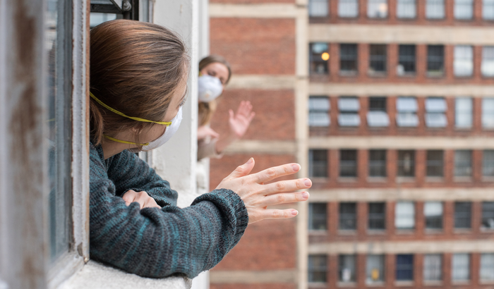 Two friends stuck at home wave to each other during Covid-19 pandemic - stock photo