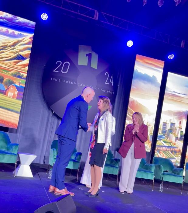 Neli Ulrich, PhD, MD, shakes hands with Gov. Spencer Cox while receiving her award at the One Utah Summit