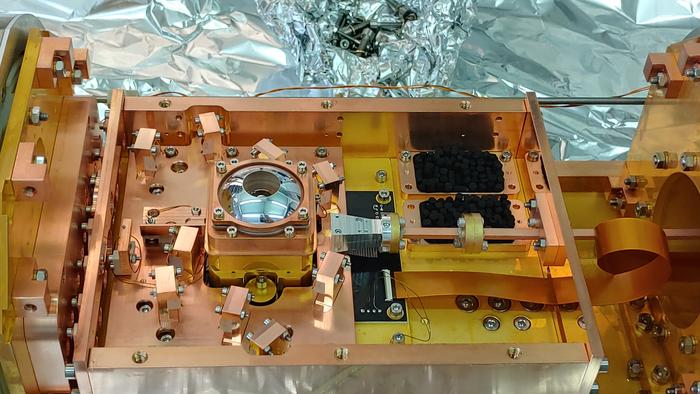 The experimental setup of the ETH researchers. The trap chip is located inside the container underneath the silver cupola, in which a lens captures the light emitted by the trapped ions.