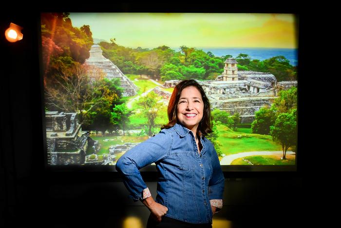 Photo of Lisa Lucero standing in front of a photo of the remains of an ancient Maya city.