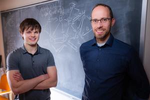 Iowa State senior Addison Schmidt (left) and associate professor of mathematics Claus Kadelka (right) stand in front of a chalk board with depictions of a gene regulatory network in Carver Hall.