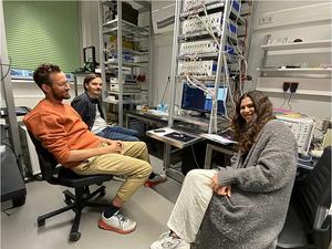 Fig. 3: The three first authors of the paper - Noura Zenbaa (on the right), Claas Abert (on the left) and Fabian Majcen (in the middle) at the moment when the universal inverse-design magnonic device was activated to solve its first problem.