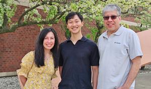 Three individuals in front of brick wall and tree